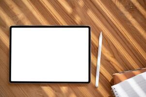 Top view image of a digital tablet mockup on a wooden table with a tablet pen and stationery. photo