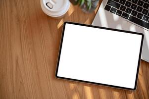 A wooden desk with a digital tablet mockup, a tablet pen, a coffee cup, and a laptop computer. photo