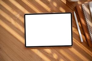 Top view image of a digital tablet mockup on a wooden table with a tablet pen and stationery. photo