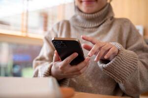 Cropped shot of a woman is checking messages on her phone while working remotely at a cafe. photo