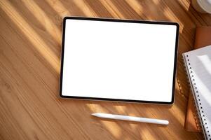 Top view image of a digital tablet mockup on a wooden table with a tablet pen and stationery. photo