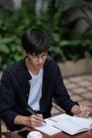 A dissatisfied and unhappy Asian man is working on his tasks at a table outdoors. photo