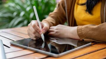 A cropped image of an Asian woman sits at an outdoor table and uses her digital tablet. photo