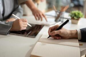 A businessman is taking notes on a notebook while having a meeting with his team in the office. photo