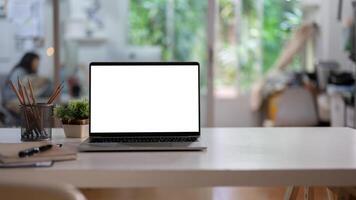 A white-screen laptop computer mockup and accessories on a white desk in a modern office. photo