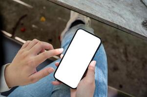 A woman in jeans relaxing at a table in a garden on a bright day, using her smartphone. photo