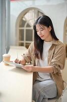un joven hermosa asiático mujer en casual vestir es sentado en un café y utilizando su digital tableta. foto