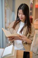 A young beautiful, positive Asian woman reading a book in a modern coffee shop in the city mall. photo