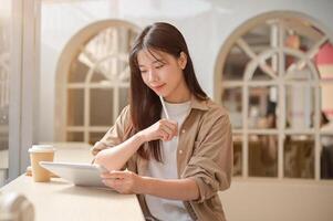 un joven hermosa asiático mujer en casual vestir es sentado en un café y utilizando su digital tableta. foto