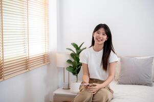 An attractive young Asian woman is sitting on bed in her bedroom and smiling at the camera. photo
