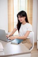 An attractive Asian woman working remotely from home, working on her laptop computer in her room. photo
