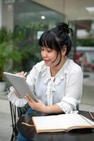 un mujer es trabajando remotamente desde un café comercio, utilizando un aguja bolígrafo en su digital tableta. foto