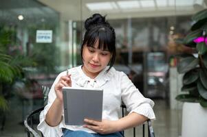 un joven asiático mujer leyendo alguna cosa en su digital tableta, trabajando remotamente desde un café tienda. foto