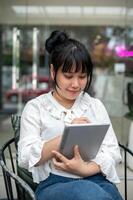 un mujer es trabajando remotamente desde un café comercio, utilizando un aguja bolígrafo en su digital tableta. foto