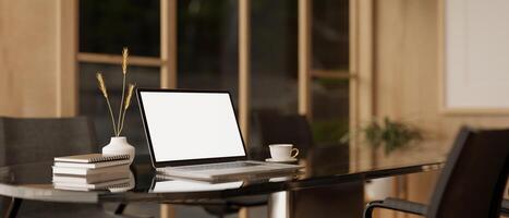 A white-screen laptop computer mockup and accessories on a meeting table in a modern meeting room. photo
