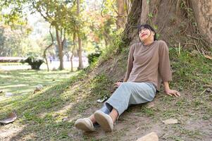 Young happy and carefree Asian woman resting under a tree in a park. photo