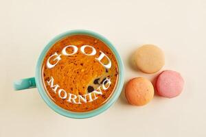 Multi-colored macaroons of different colors and flavors on a beige background with a cup of coffee. View from above photo