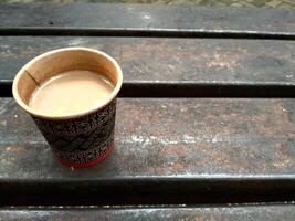 Paper Cup of Coffee on Bench in Outdoor Setting, Warm Beverage in Disposable Cup on Vintage Bench, Rustic Coffee Moment using Paper Cup on Outdoor Bench With copy space for text quotes photo