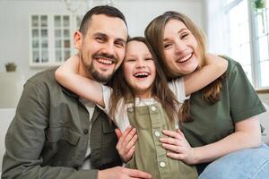 Happy family at home. Mother father children daughter relaxing on sofa indoor. Mom dad parents kid girl relax playing hugging having fun together. Family smiling laughing enjoying tender moment photo