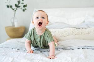 contento bebé. linda pequeño recién nacido niña con sonriente cara gateando en cama en dormitorio. infantil bebé descansando jugando acostado abajo en cobija a hogar. maternidad contento niño cuidado de niños concepto foto