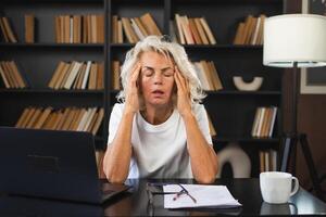 Headache pain. Middle aged woman touching temples experiencing stress. Mature old lady tired of work feeling headache sick rubbing temples forehead. Long laptop usage computer vision office syndrome photo