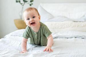 contento bebé. linda pequeño recién nacido niña con sonriente cara gateando en cama en dormitorio. infantil bebé descansando jugando acostado abajo en cobija a hogar. maternidad contento niño cuidado de niños concepto foto
