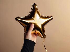 A golden star-shaped foil balloon held by a single hand, set against a beige background. photo