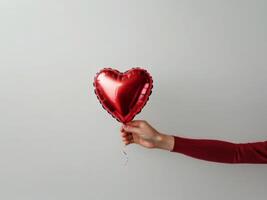 A red heart-shaped foil balloon held by a hand, isolated on a neutral background photo