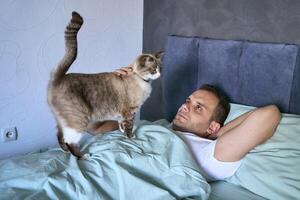a young man sleeping with a cat on his chest, morning routine photo
