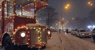 Heavy snowfall on Christmas evening against the backdrop of a red bus double decker. 4K video