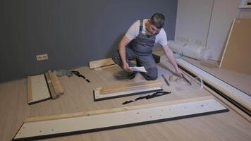 A builder in a work overalls is assembling a bed. Assembling furniture in a new apartment. video
