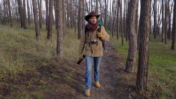 A man with a guitar and a camera walks along a trail in the forest. Travel concept. Slow motion video