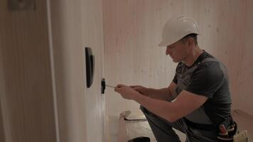 Electrician installing an electrical outlet in a new home construction. He carefully uses tools and techniques to ensure a safe and functional installation. The cabin has a natural wood interior. video