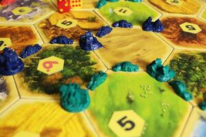 Mozyr, Belarus, April 01 2024. A catan board game green and blue chips of players on the field. Rivalry for hexes and resources between players. Cities and settlements in the game photo