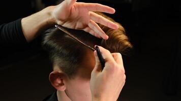 Closeup View Of barber using hair clip and comb to fix hair for cut and styling it Hairdresser use pinsn hair salon. service in a modern barbershop in a dark key lightning with warm light back view photo