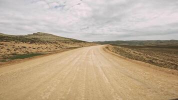 A car gracefully meanders down a dusty desert road, surrounded by vast sandy landscapes and towering mountains, showcasing the majestic beauty of the arid wilderness video