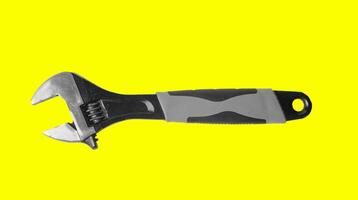 Mechanic with wrench, adjustable spanner in hand on yellow background. Old steel tools, mechanical photo