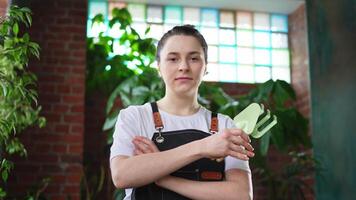 Running of own business. Young woman florist wearing apron in botanical store with green plants. Happy small business owner working at flower shop standing surrounded by plants. Small business video