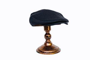 Concept photo of a classic flat cap or scally cap made of warm wool. Classic black hat mounted on bronze mannequin head on white studio background