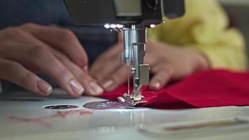 Close-up of a sewing machine slowly stitching a piece of red fabric with a large needle. Slow motion video