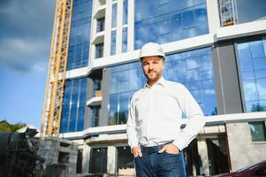Successful engineer or architect, crane and building construction at backgrpound. Joyous businessman wearing helmet photo