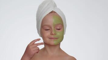 Beautiful smiling child girl kid in towel on head applying cleansing moisturizing green mask on face video