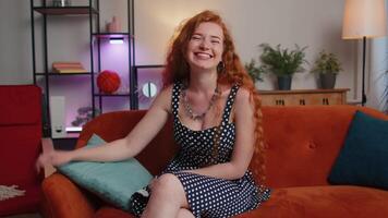 Redhead girl smiling friendly at camera, waving hands gesturing hello, hi, greeting at home on couch video
