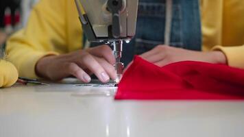 Front view of a tailor carefully embroidering a seam on a piece of red satin fabric for a future dress. Close up. Slow motion. video