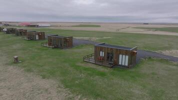 Aerial view of the vast green fields in Iceland with cozy lodges and mountains in the background. A wooden cabin in the middle of nowhere. video