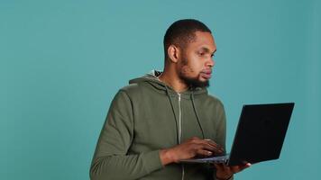 Man typing on laptop keyboard, checking emails, feeling overjoyed after receiving good news. Employee sending mail online, celebrating after meeting KPIs at work, studio background, camera A video
