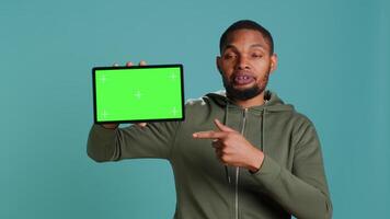 Tech content creator holding isolated screen tablet, doing promotion, talking with audience. Man pointing towards chroma key digital device, doing advertising, studio backdrop, camera A video