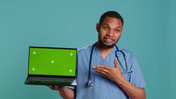 Portrait of african american doctor in medical scrubs using isolated screen laptop. Hospital staff member doing presentation using chroma key notebook, showing patient treatment plan, camera A video