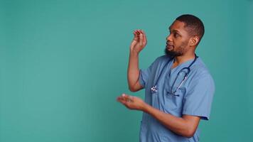 Male nurse pointing finger towards empty space doing advertising, talking with audience. Healthcare worker doing presentation, showing copy text, studio backdrop, camera B video