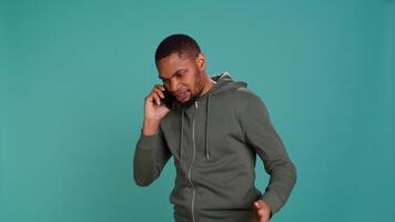 Irked african american man fighting with friends during telephone call, isolated over studio background. Outraged person arguing with mates during conversation on mobile phone, camera B video